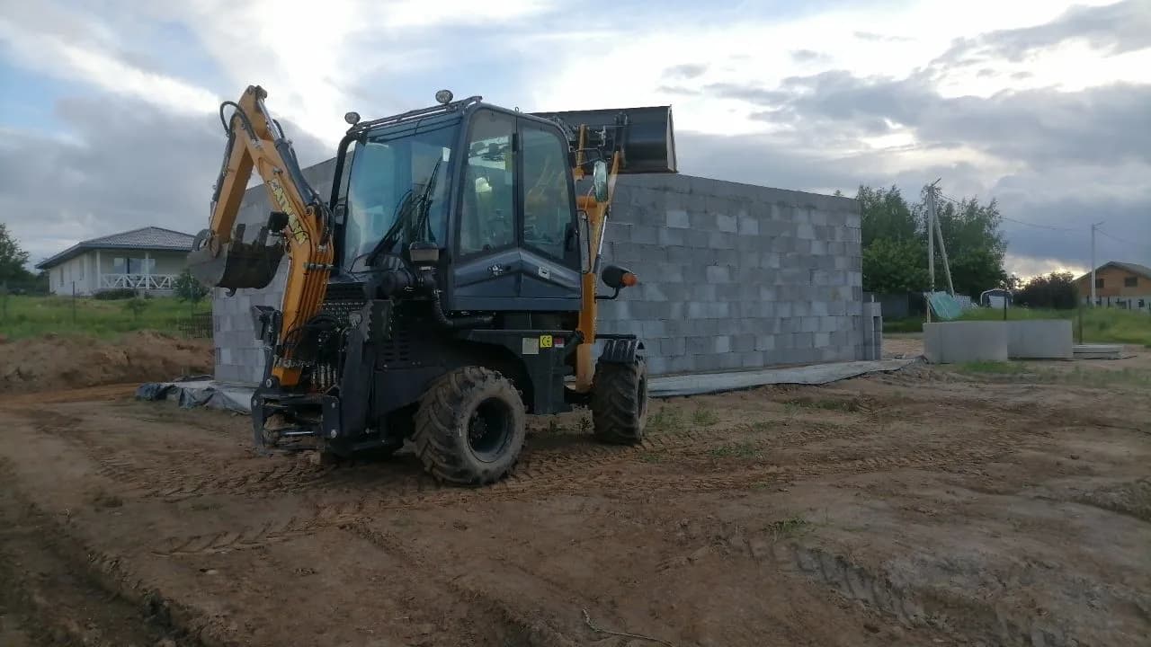 Мини-экскаватор-погрузчик CAT 504 возле строящегося дома